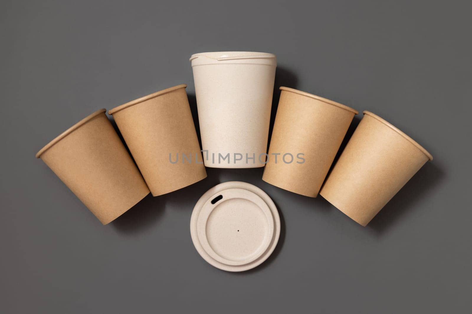 Disposable new beige kraft paper cups and opened reusable bamboo coffee cup with a lid on gray top view, mockup with copy space. Empty coffee cups. No plastic and sustainable lifestyle concept