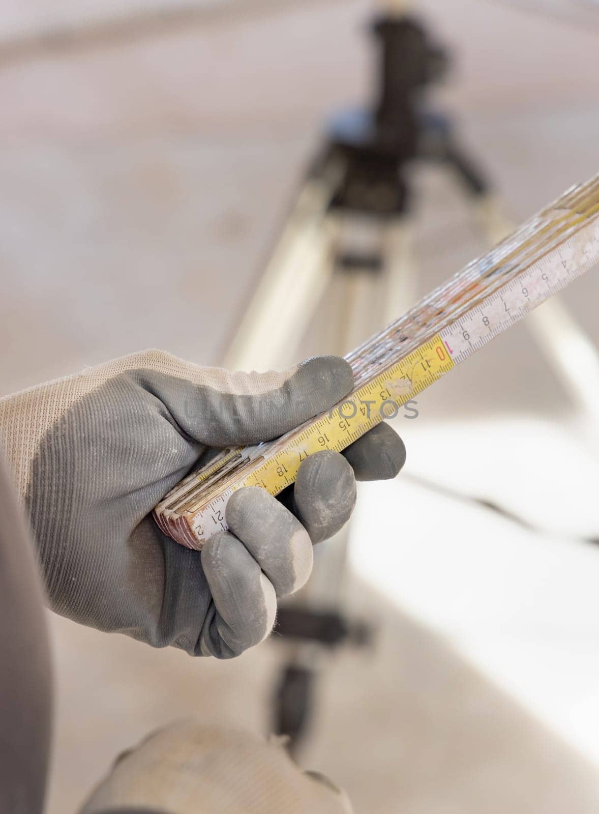 Craftsman in dusty glove holding a folded rule against horizontal rotary laser level. Engineer during measurement work, construction or renovation site