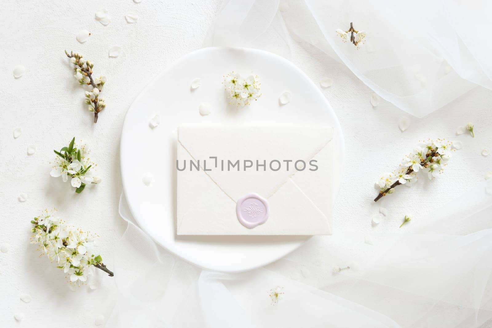 Sealed envelope on plate near tulle and wild plums white flowers top view, mockup. Pastel horizontal card for spring party design, mothers day or romantic wedding stationery
