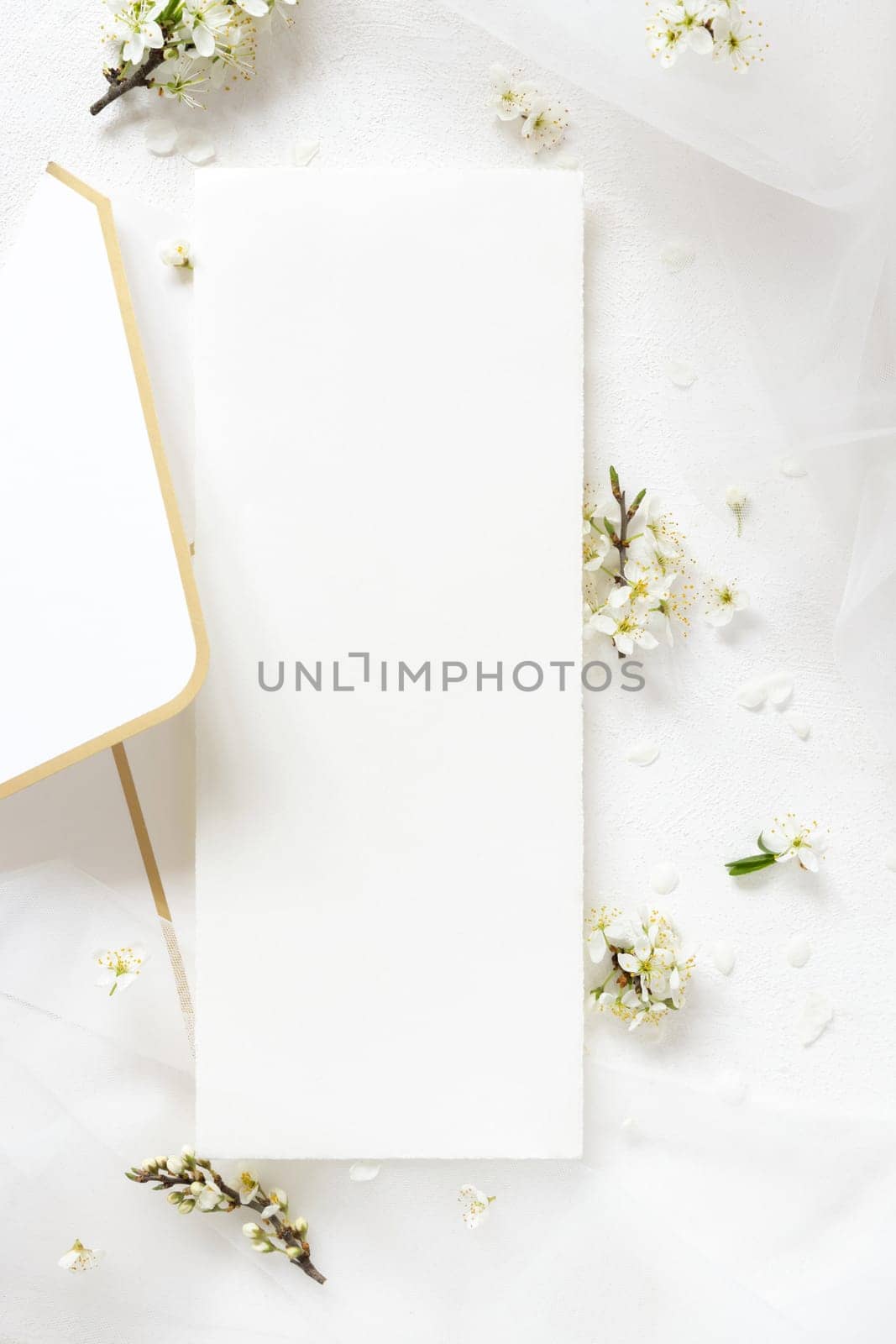 Blank menu card on envelope near tulle and wild plums white flowers top view, mockup. Pastel vertical card for spring party design or romantic wedding stationery, Close to nature or mothers day