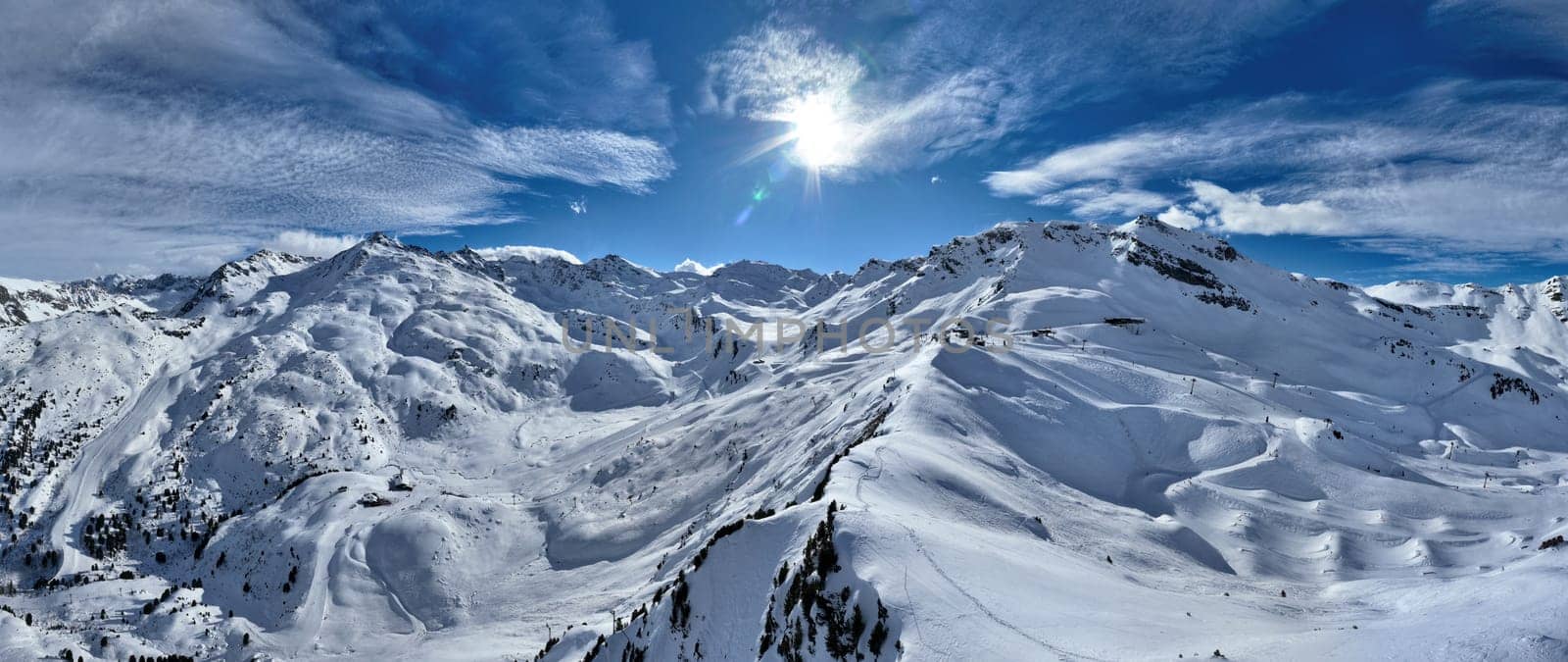 A breathtaking aerial view of a beautiful winter landscape with snow-covered alpine mountains, sunny skies, and scenic slopes perfect for skiing, snowboarding, hiking, and outdoor adventures