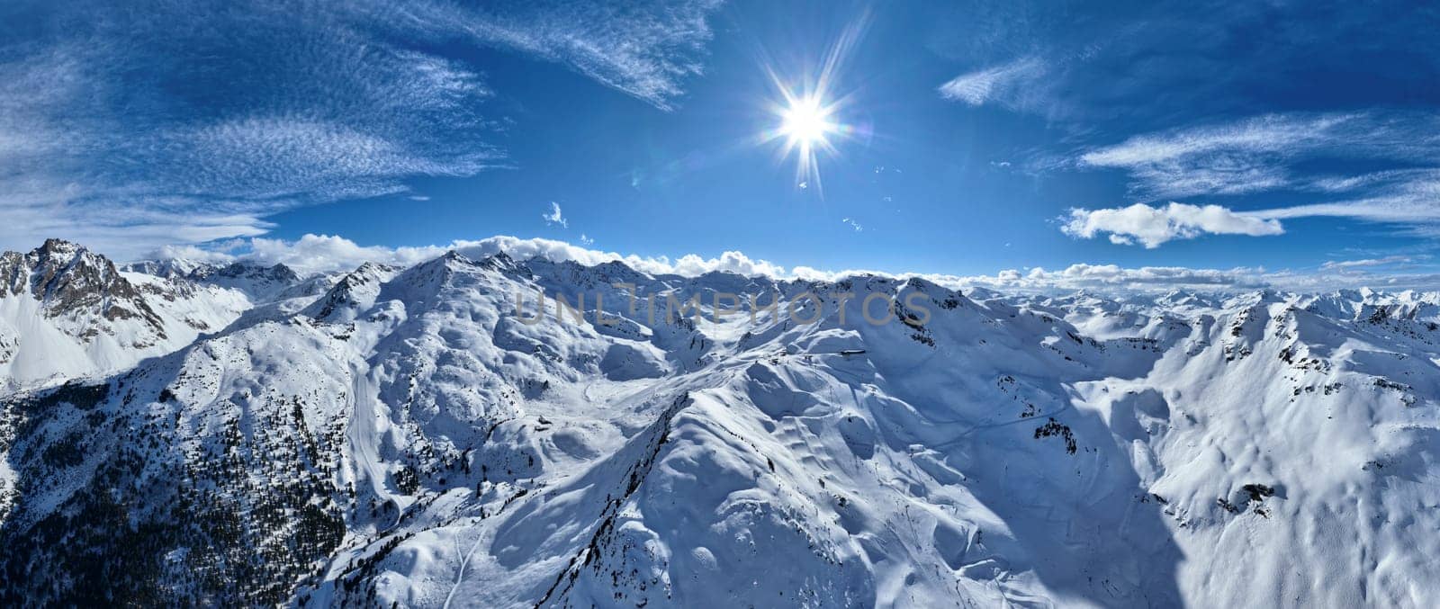 A breathtaking aerial view of a beautiful winter landscape with snow-covered alpine mountains, sunny skies, and scenic slopes perfect for skiing, snowboarding, hiking, and outdoor adventures