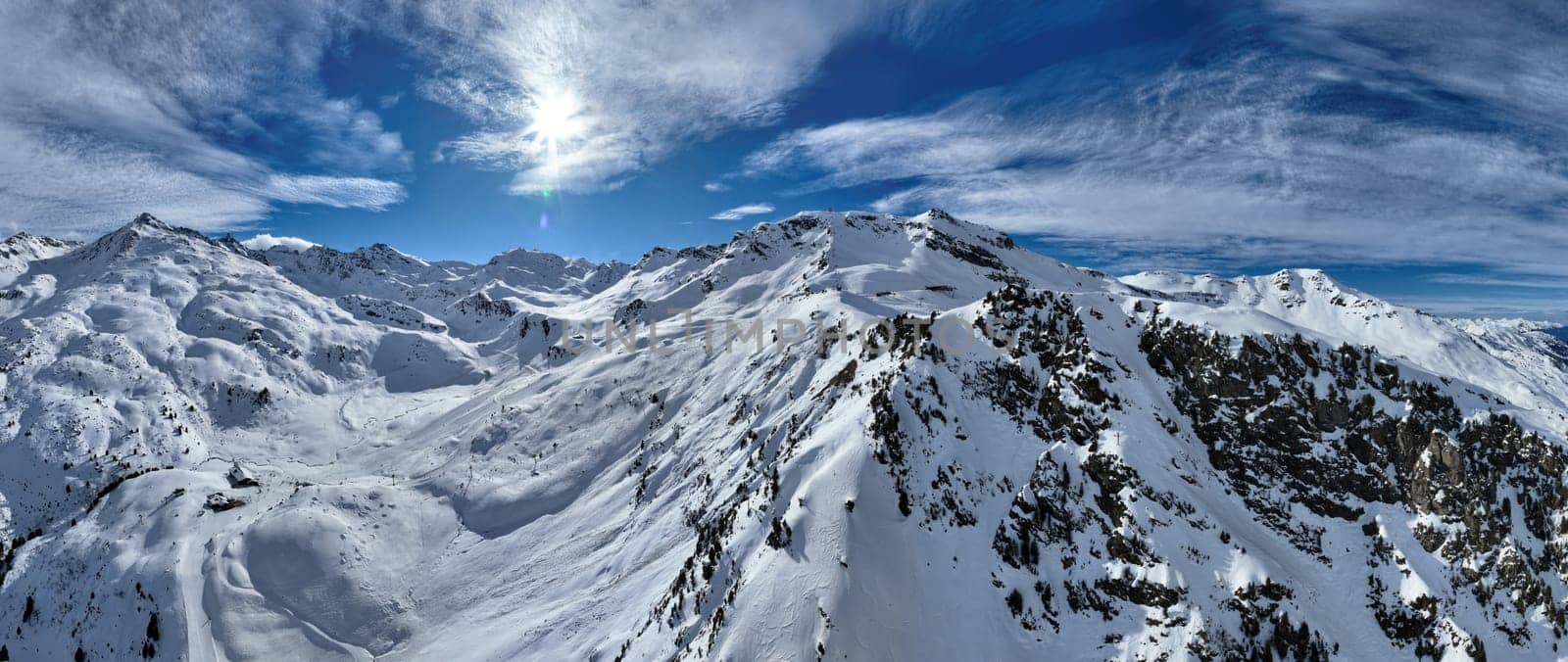A breathtaking aerial view of a beautiful winter landscape with snow-covered alpine mountains, sunny skies, and scenic slopes perfect for skiing, snowboarding, hiking, and outdoor adventures