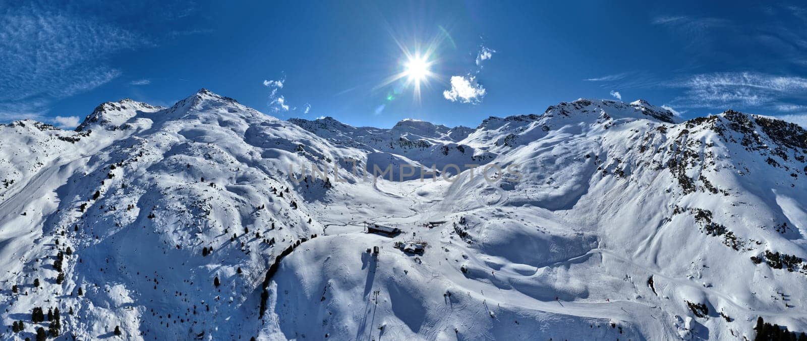 A breathtaking aerial view of a beautiful winter landscape with snow-covered alpine mountains, sunny skies, and scenic slopes perfect for skiing, snowboarding, hiking, and outdoor adventures