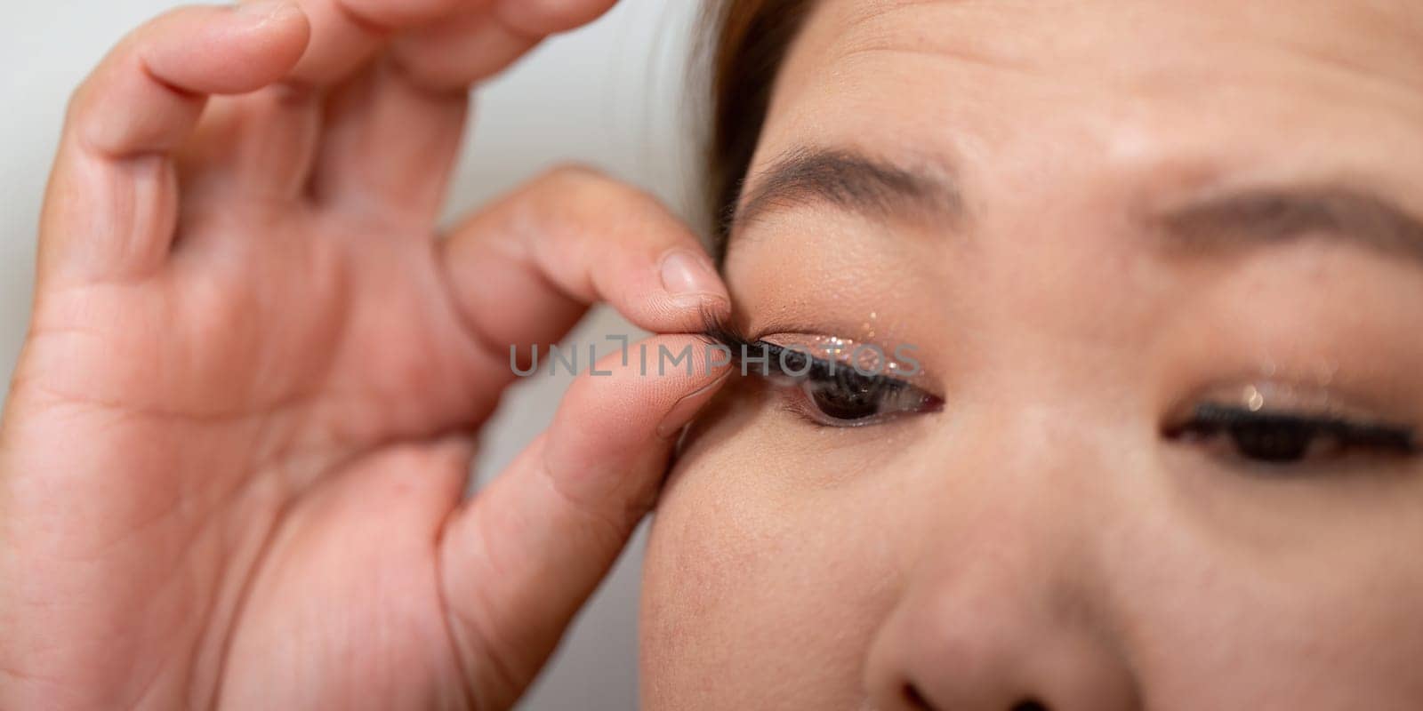 A beauty enthusiast carefully applies false lashes, focusing on enhancing her eye makeup for a captivating look in her daily routine.