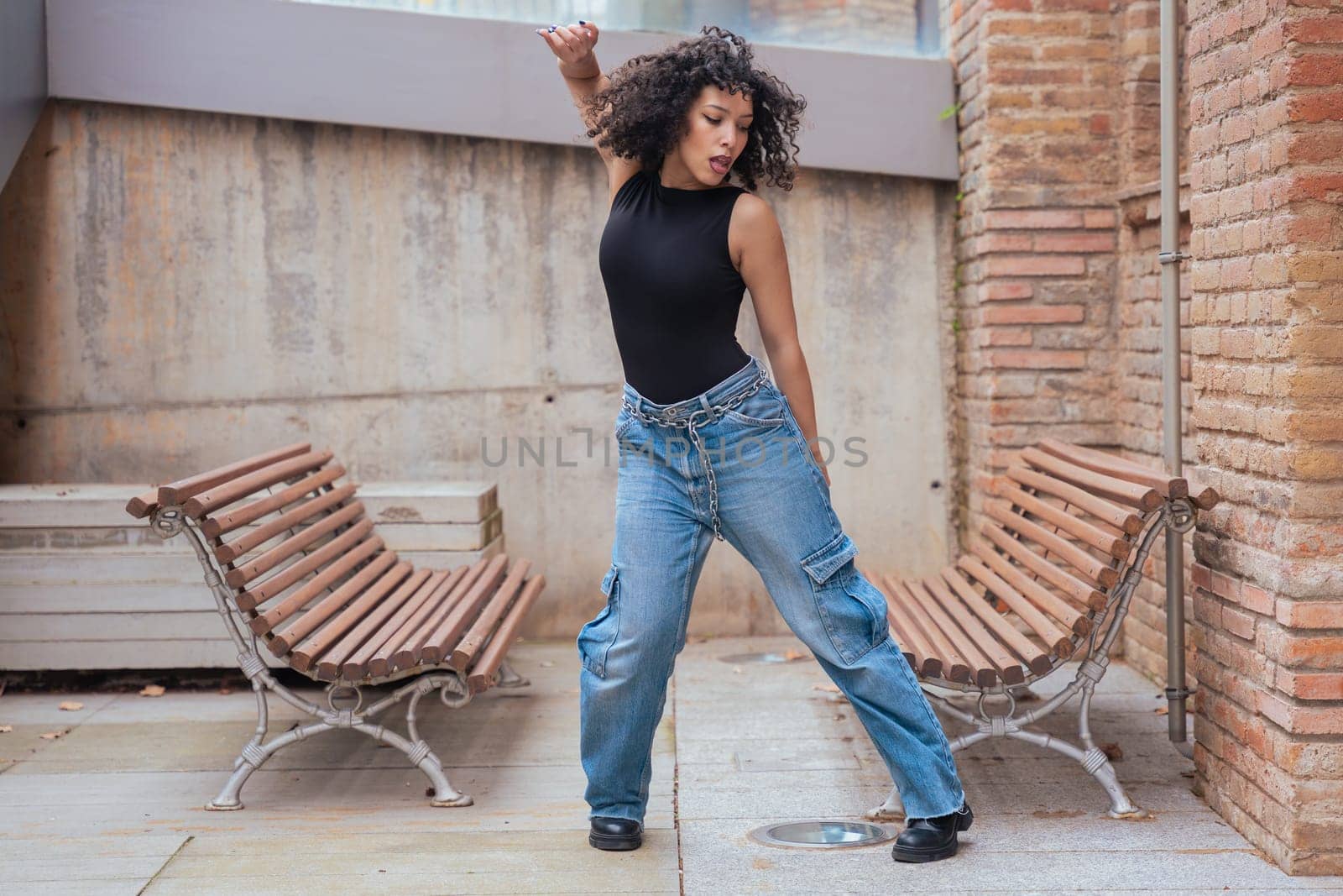 African American woman dancing in a creative pose between benches in an urban setting. She wears casual clothes and shows balance, strength, and expression. Concept of movement, art, and freedom.