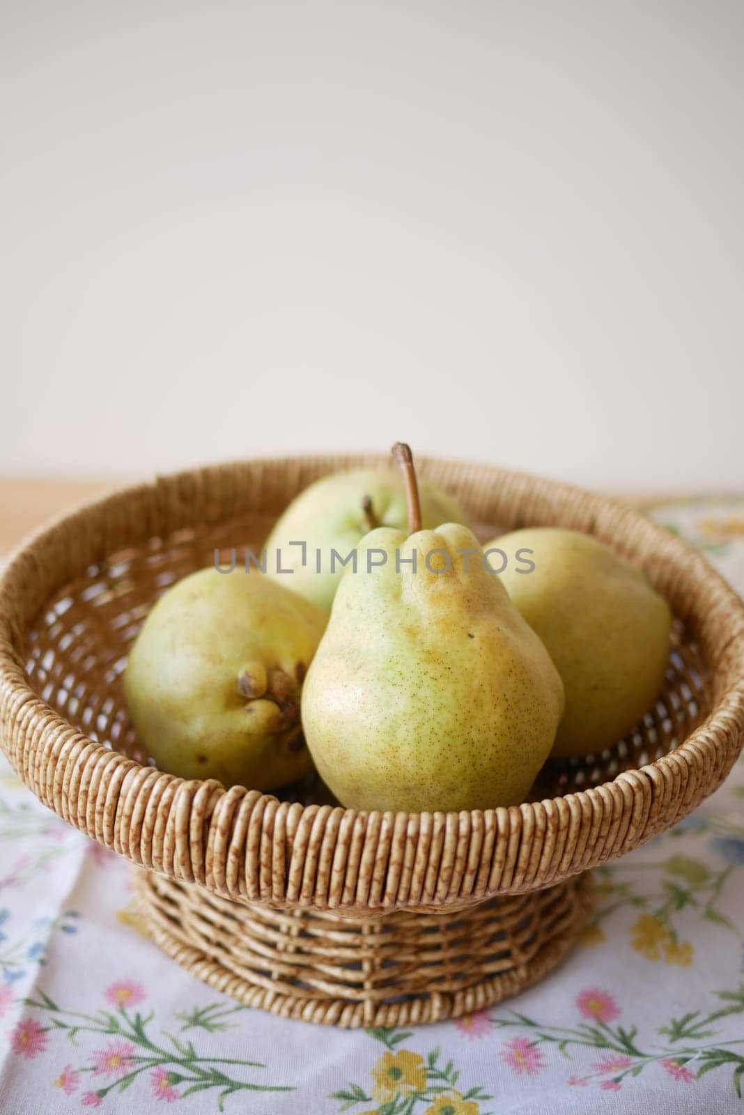 Fresh pears are neatly displayed in a woven basket on a patterned cloth.