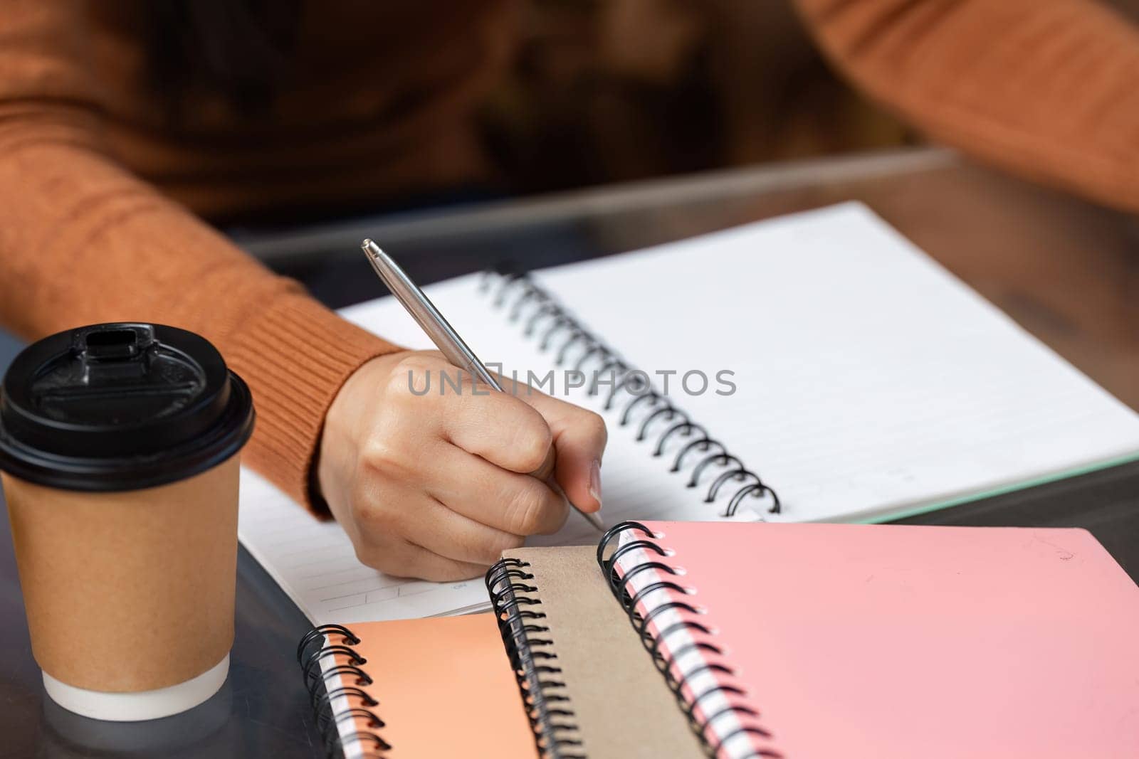 In a cozy cafe corner, a student takes notes while sipping coffee, capturing ideas for an upcoming project, embodying dedication and inspiration.