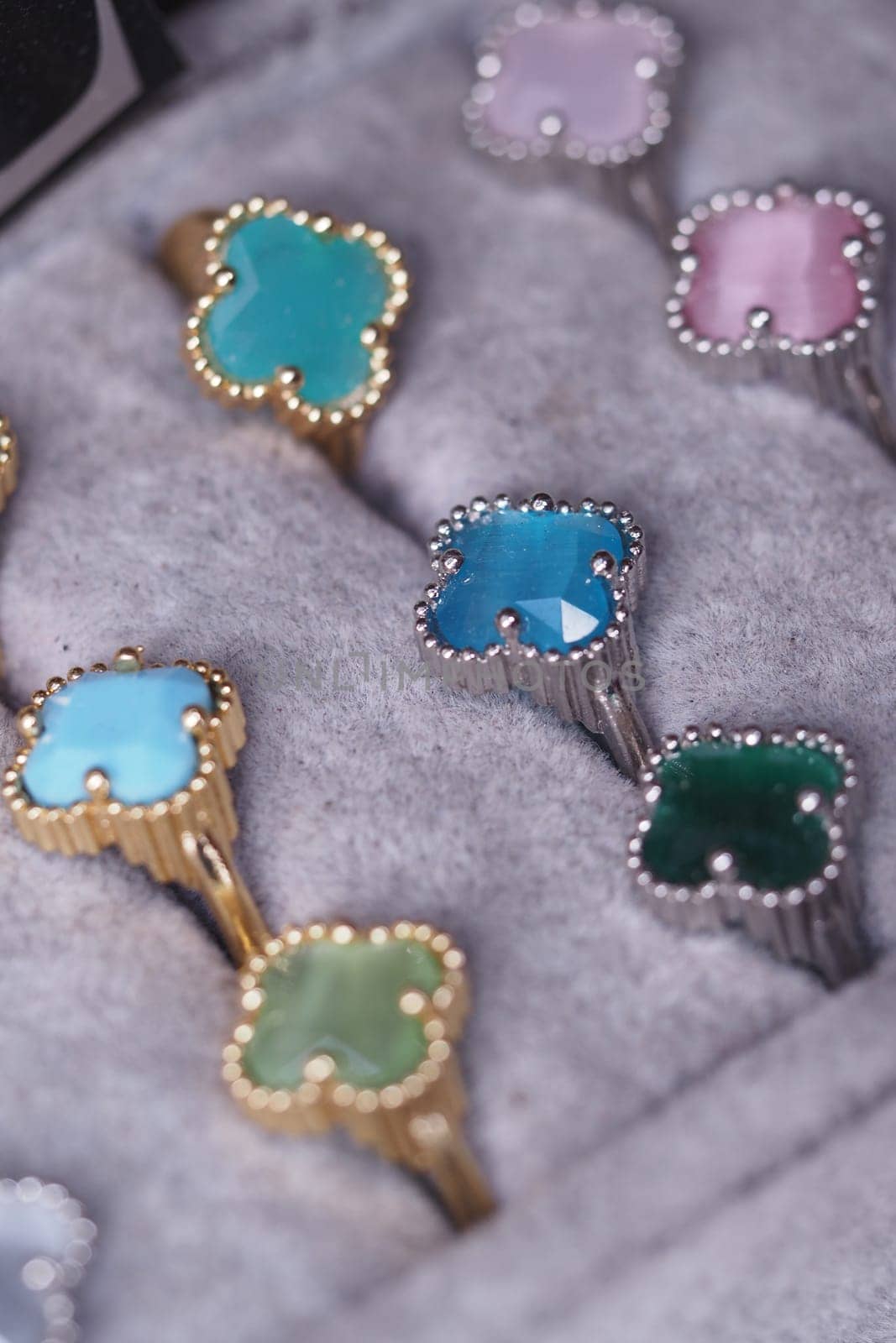 Various gemstone rings in shades of blue, green, and pink are neatly arranged.