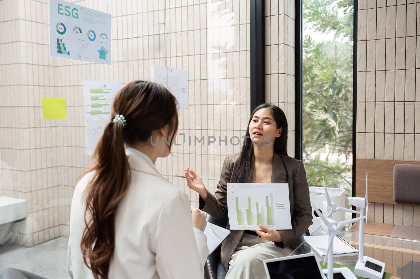 In a collaborative workspace, two professionals engage in a conversation about ESG strategies, showcasing data charts that reflect their commitment to sustainability.