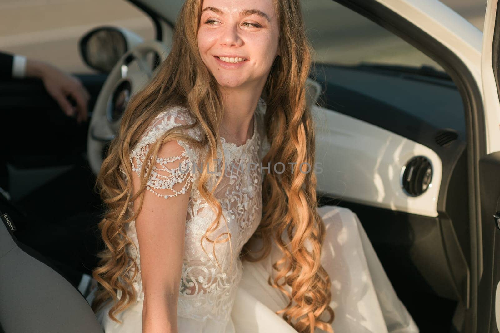 Young woman in white lace dress near car door. Wedding, elegance, femininity, movement, and soft natural beauty in everyday surroundings.