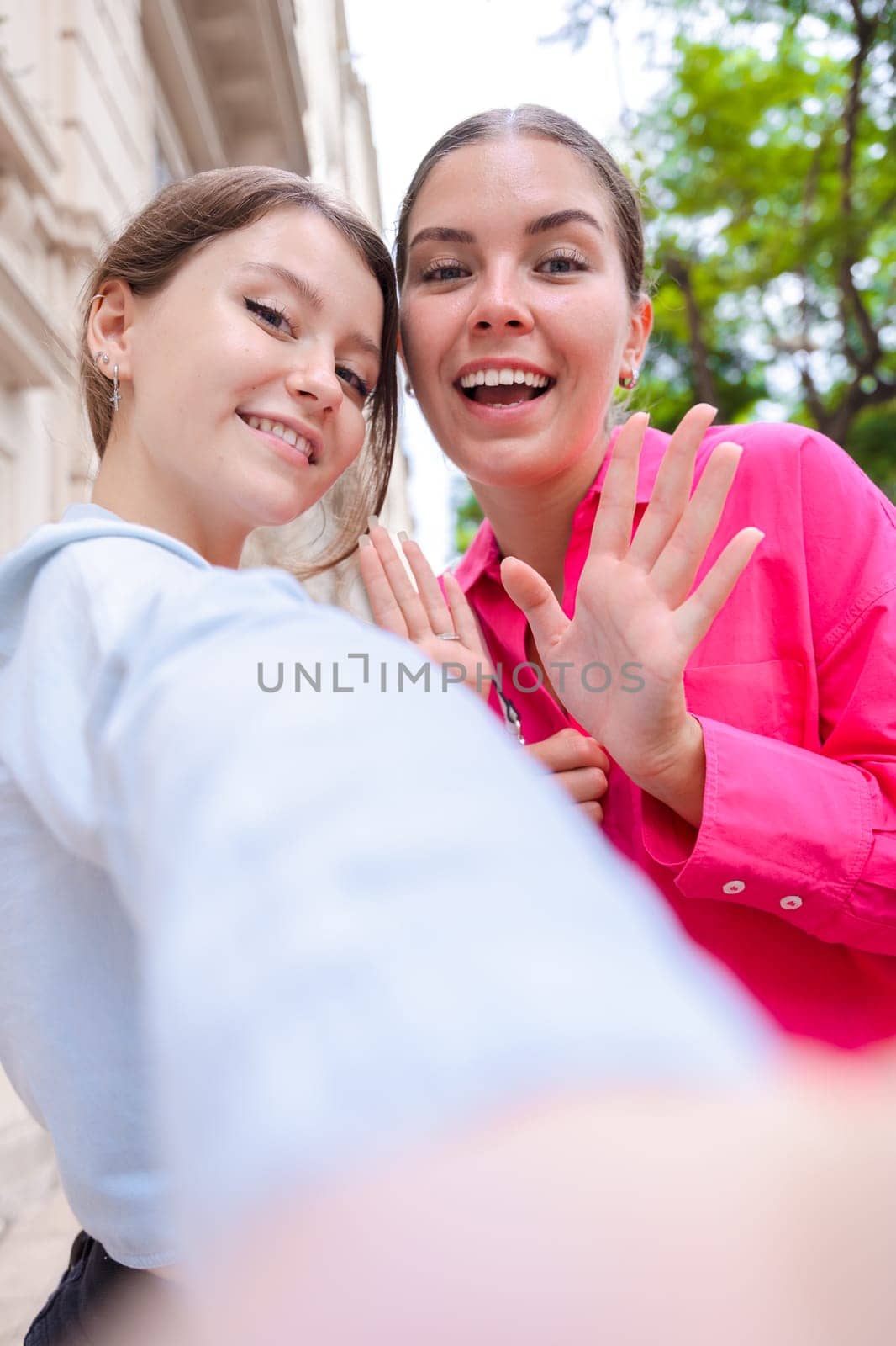 Caucasian women smiling closely while taking a selfie together on a city street. Outdoor setting with trees and buildings, capturing a joyful and candid moment of friendship and connection .Vertical