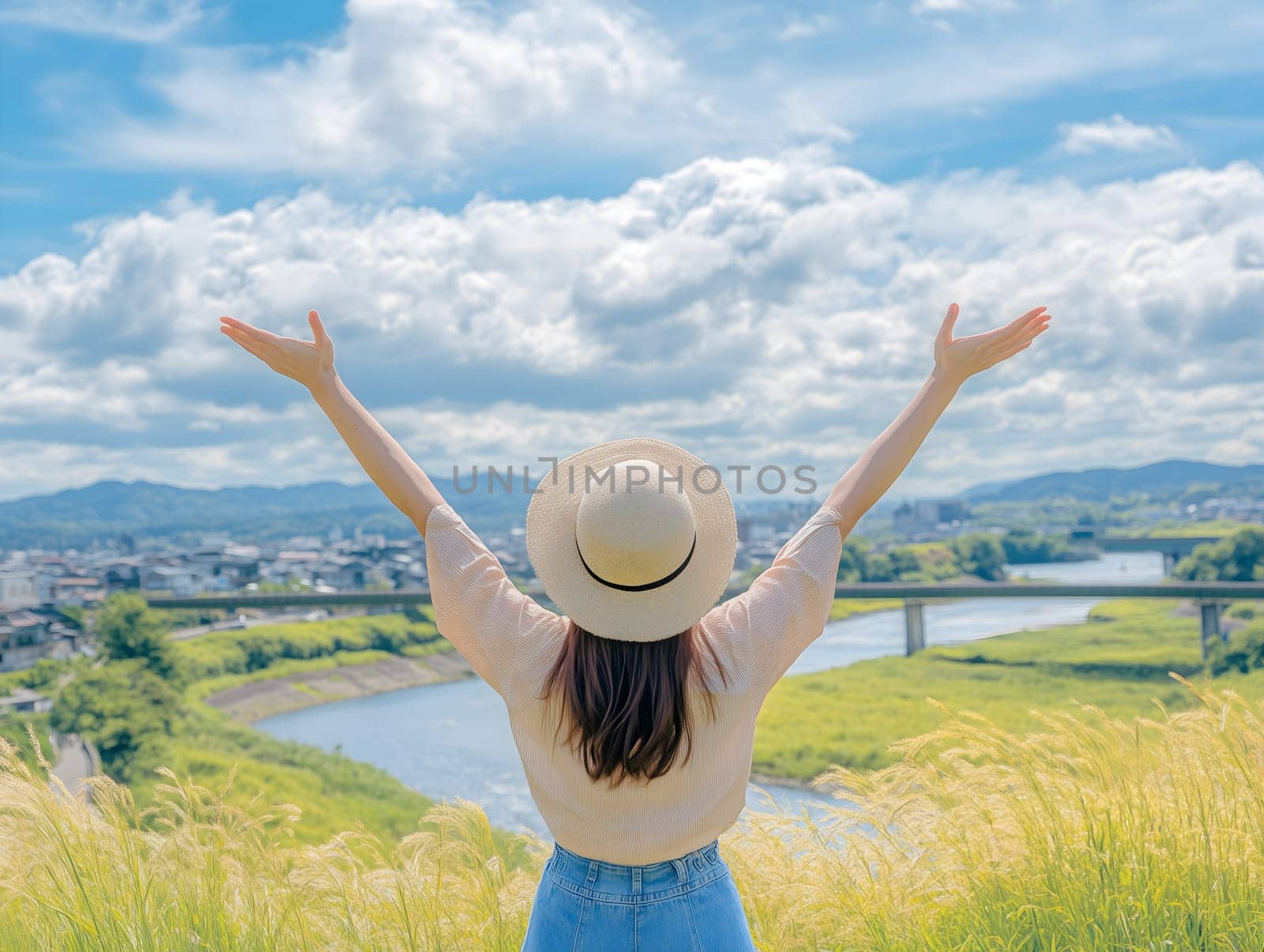 AI generated image of joyful woman standing in tall grass with arms raised, wearing hat and admiring a scenic view of river, fields and clouds under a bright summer sky