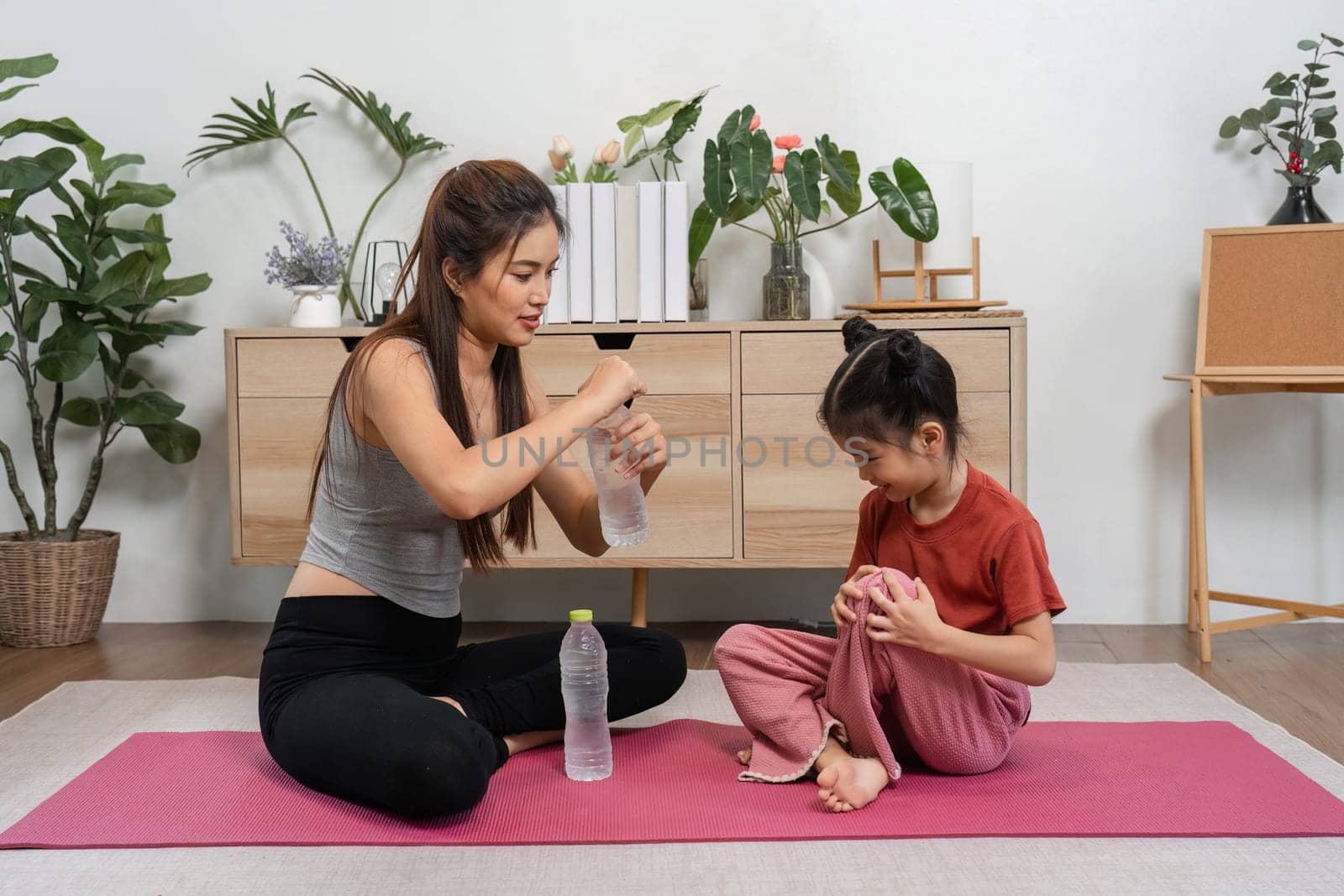 A dedicated woman shows a young girl the significance of hydration during their exercise session, fostering a love for fitness and healthy habits.