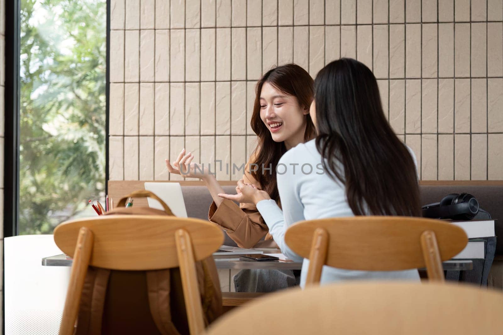Two young women engaged in vibrant conversation, sharing academic insights and working together on their assignments in a lively university atmosphere.