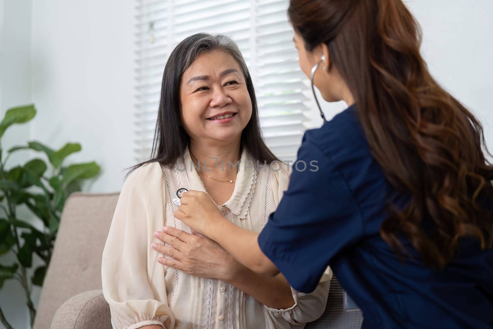 In a home setting, a compassionate caregiver attentively checks the heartbeat of an elderly woman, illustrating the bond of trust and the importance of health management.