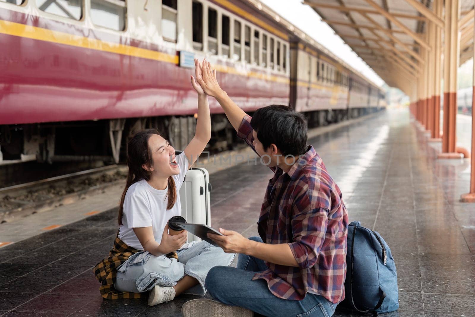Sitting on the platform, the couple high-fives each other with exuberance, enjoying their time together at the train station.