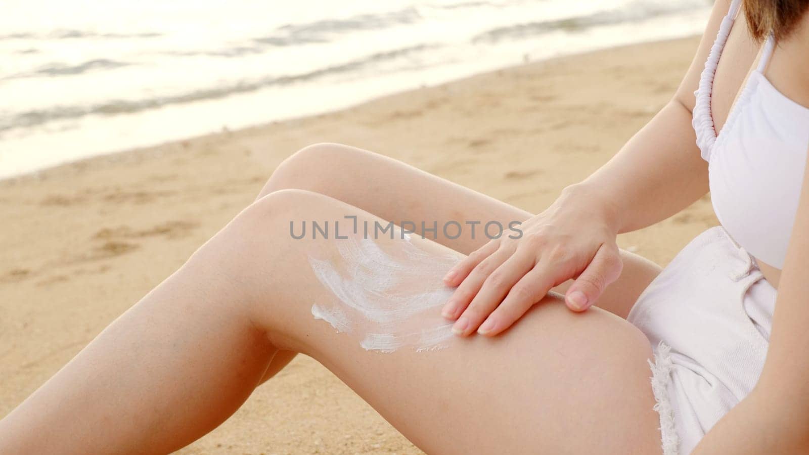 Beautiful Asian woman apply sun protection cream on tanned on leg at tropical beach with white sand, Sun Cream Skincare, Close up female in bikini using sunscreen lotion on back body before sunbathing