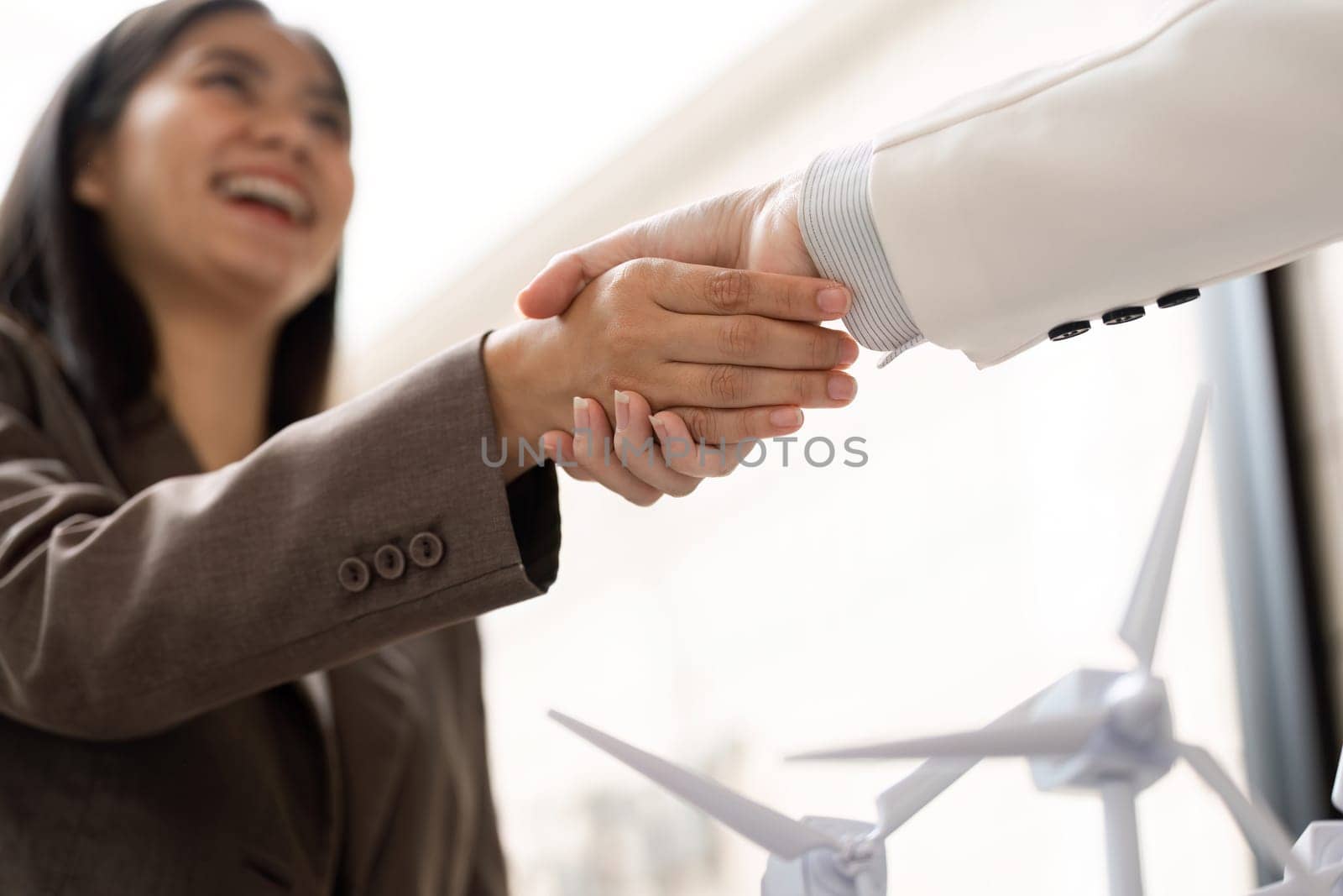Two professionals engage in a friendly handshake, representing a commitment to sustainability and ESG initiatives, with wind turbine models symbolizing their joint effort.