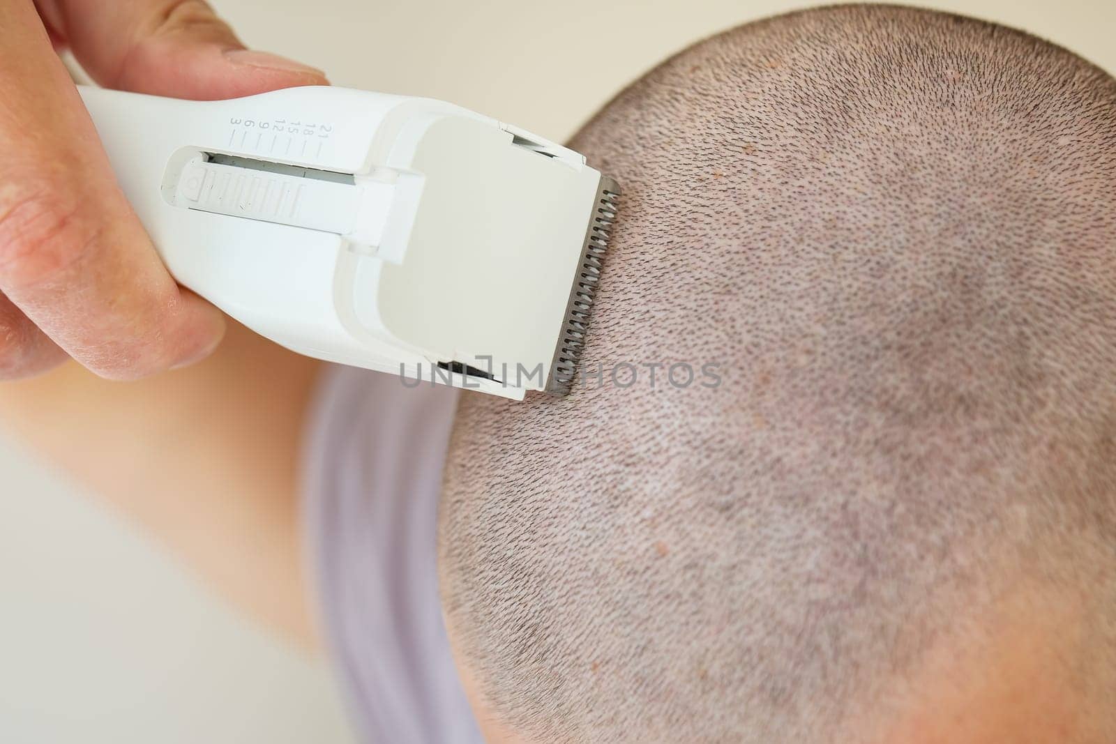 Close-up view of a person using an electric razor to shave their head, short buzz cut.