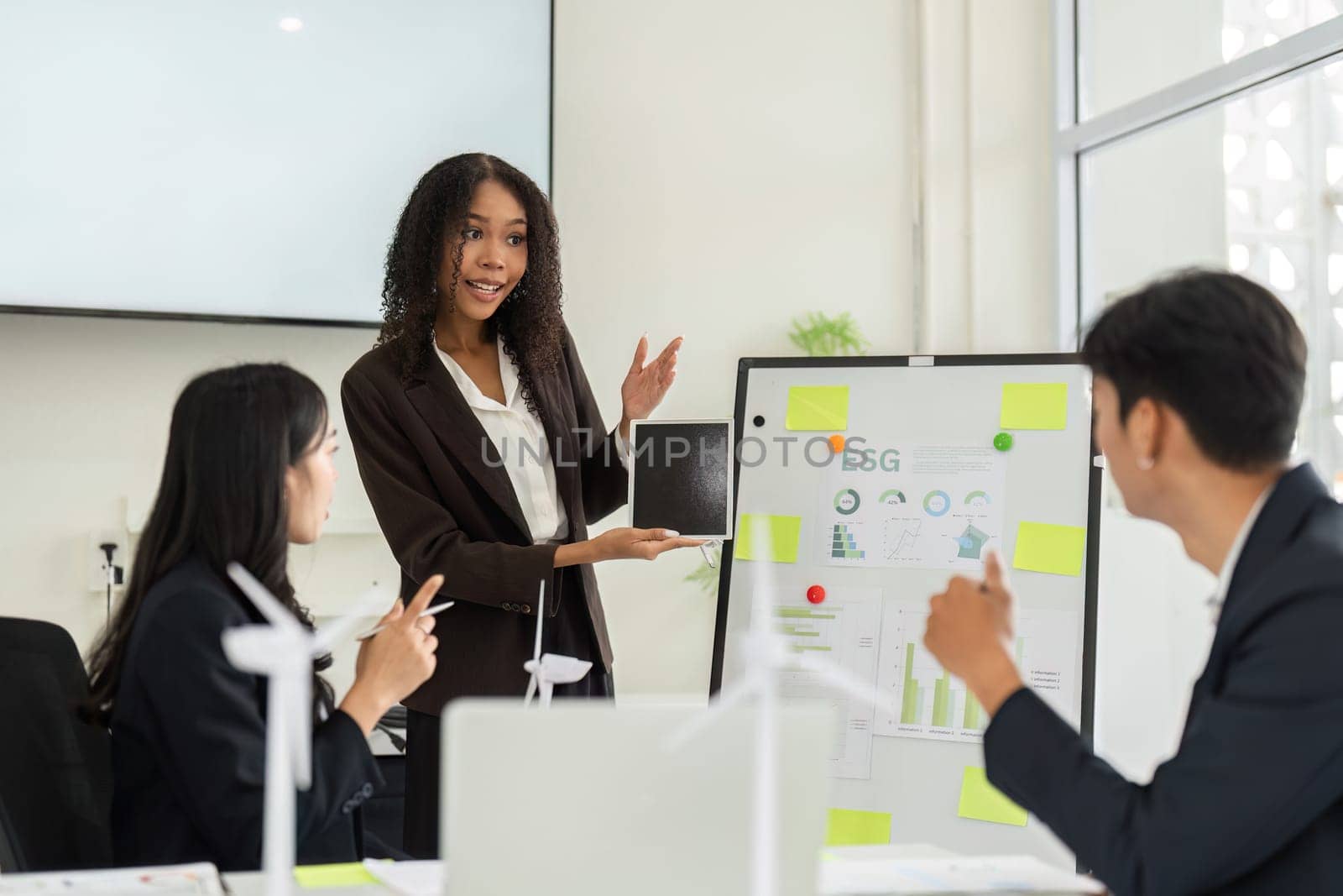 In a modern office environment, a confident presenter shares effective ESG strategies with her team, emphasizing sustainability and corporate responsibility during a meeting.