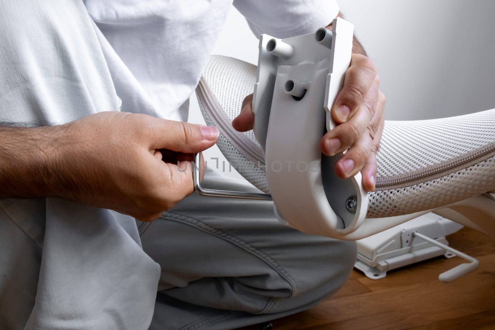 Male assembling office chair using allen wrench in bright room.