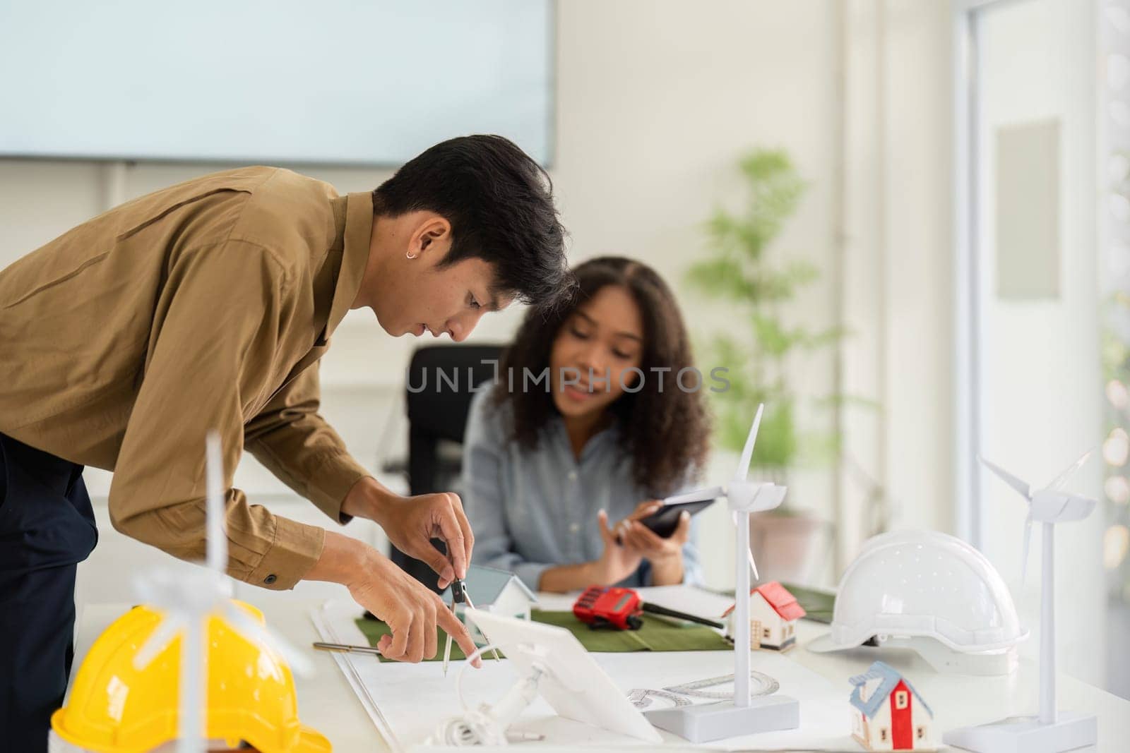 The focus is on a detailed discussion as the man sketches out a sustainable design plan while the woman provides her insights, highlighting teamwork in architecture.