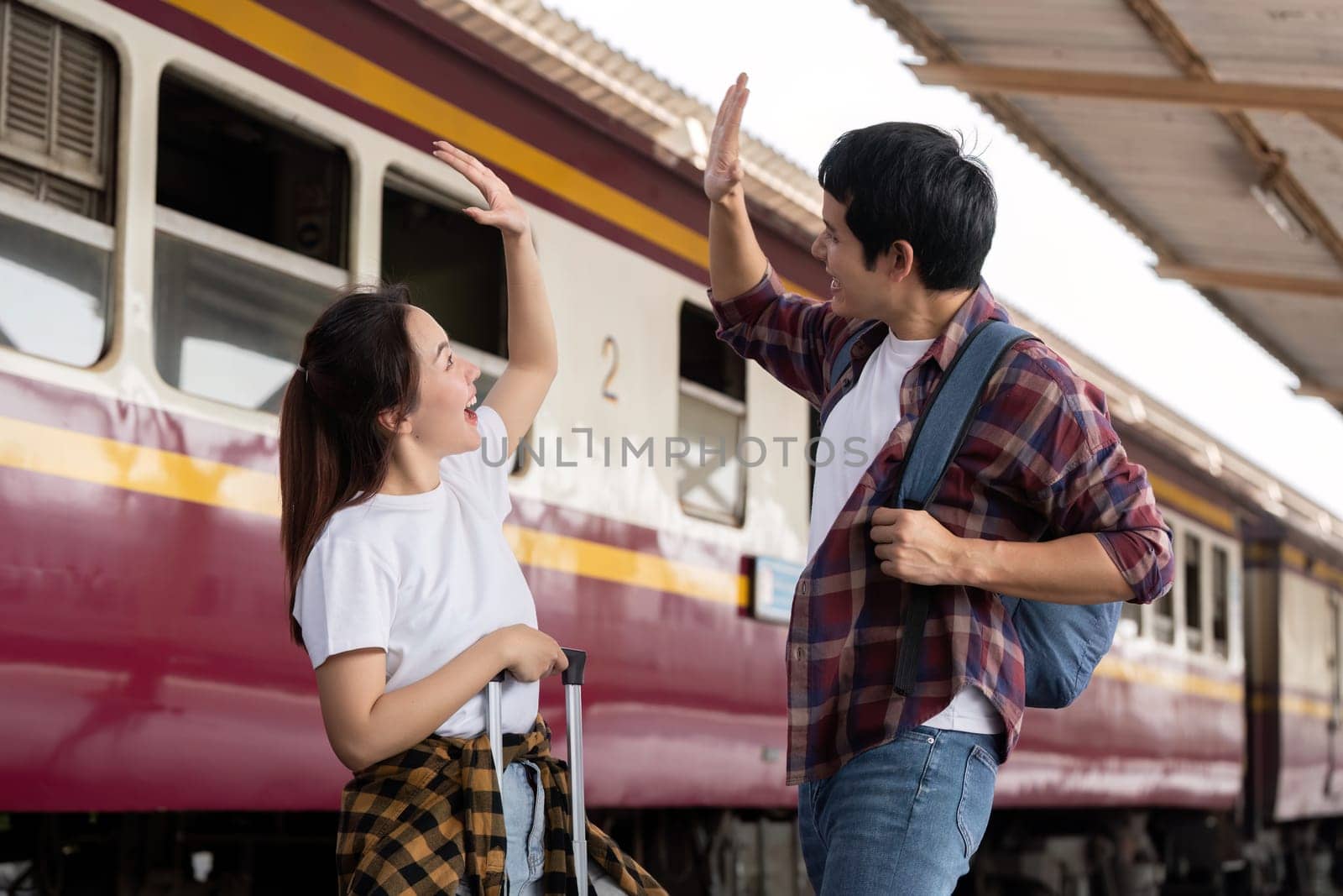 At the train station, a couple shares an enthusiastic high-five, showcasing their excitement about the adventures that await them on their trip.