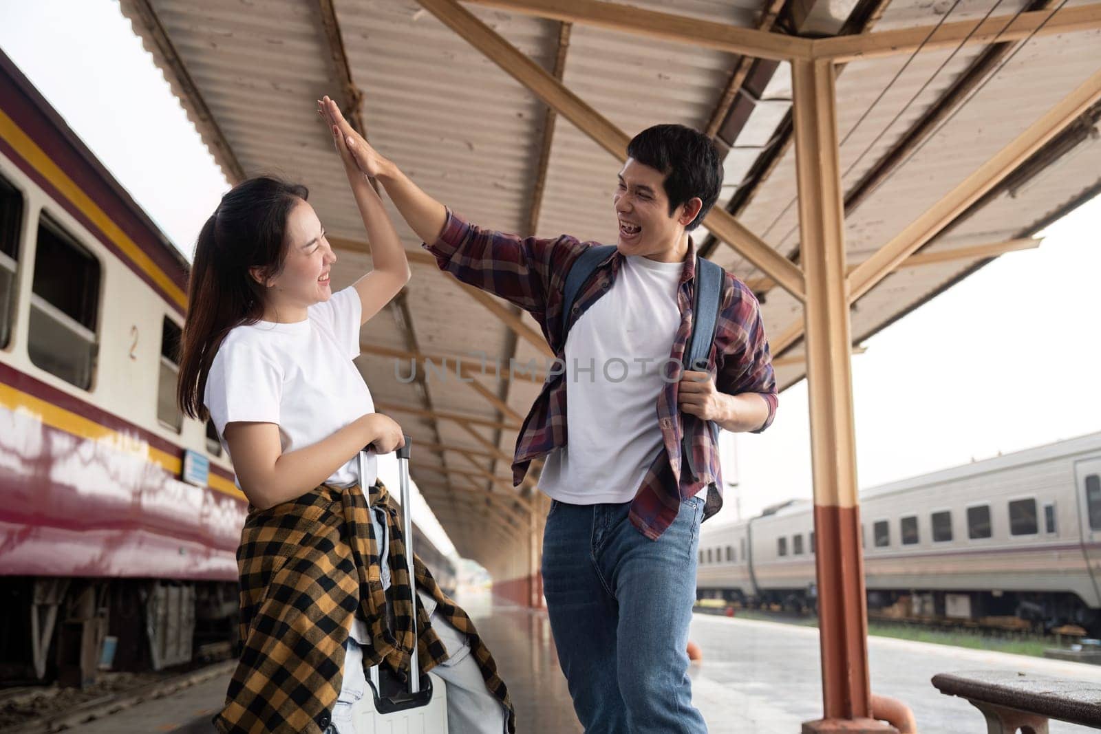 A joyful couple shares a high-five at the train station, excited about their travel plans. Their cheerful demeanor captures the essence of love and adventure.