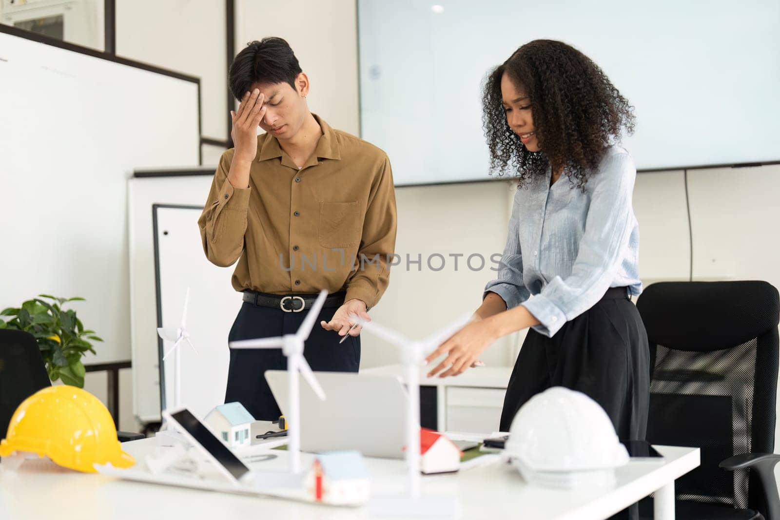 Two professionals engaged in a tense meeting about renewable energy projects, surrounded by models and tools, highlighting sustainable practices in the workplace.