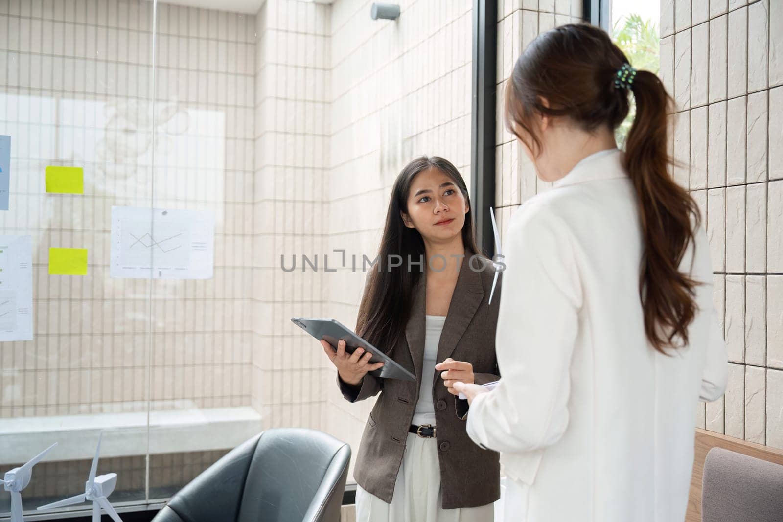 In a modern workspace, a woman presents her ESG findings, while her colleague listens intently, highlighting the importance of collaboration in promoting sustainable initiatives.