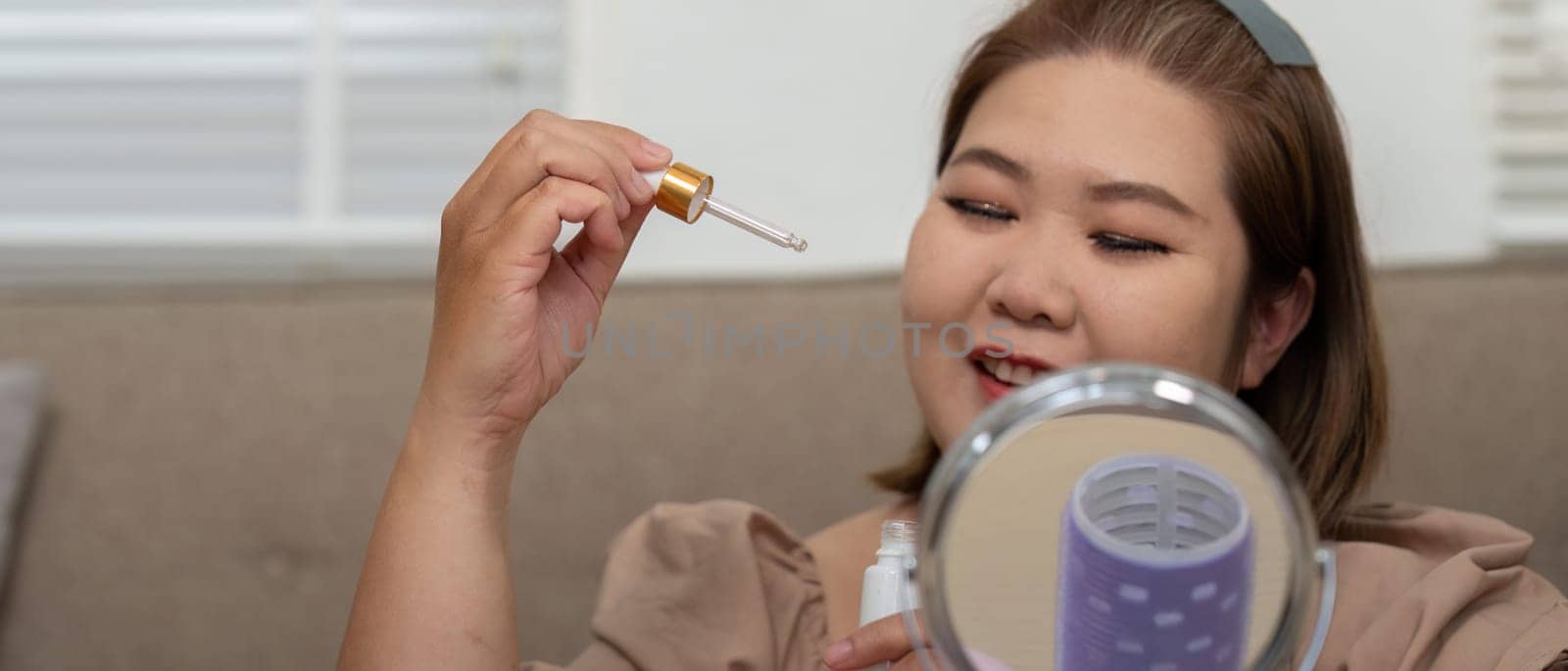 A delighted woman holds a skincare serum dropper, eagerly preparing to nourish her skin, highlighting the synergy between beauty products and self-confidence.