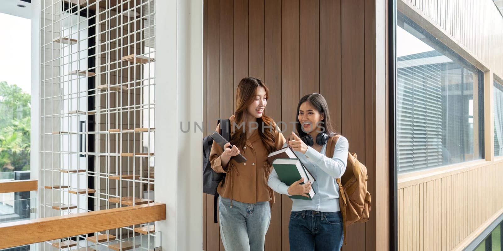 Two university friends stroll down the hallway, exchanging ideas and strategies for upcoming studies while carrying books and backpacks.