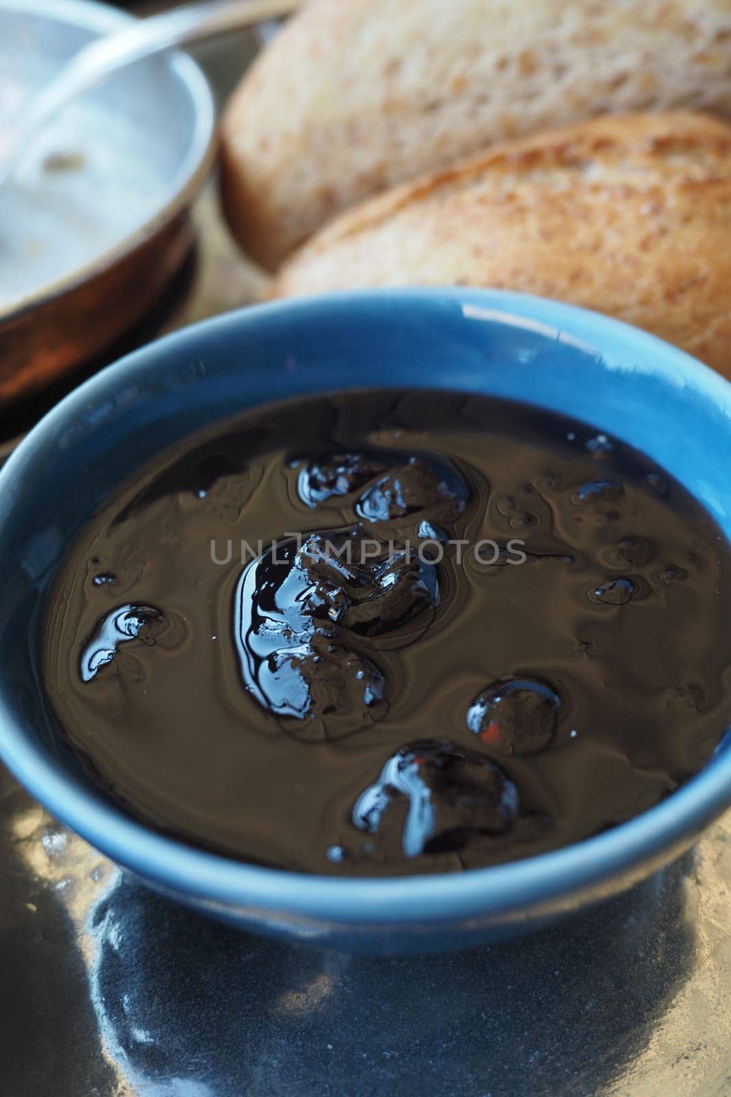 A rich dark chocolate sauce is served in a blue bowl alongside bread.
