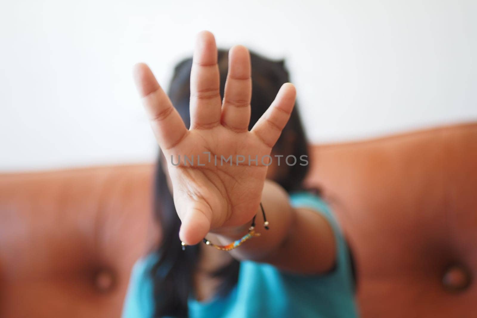 A child playfully stopping the camera with a hand gesture indoors.