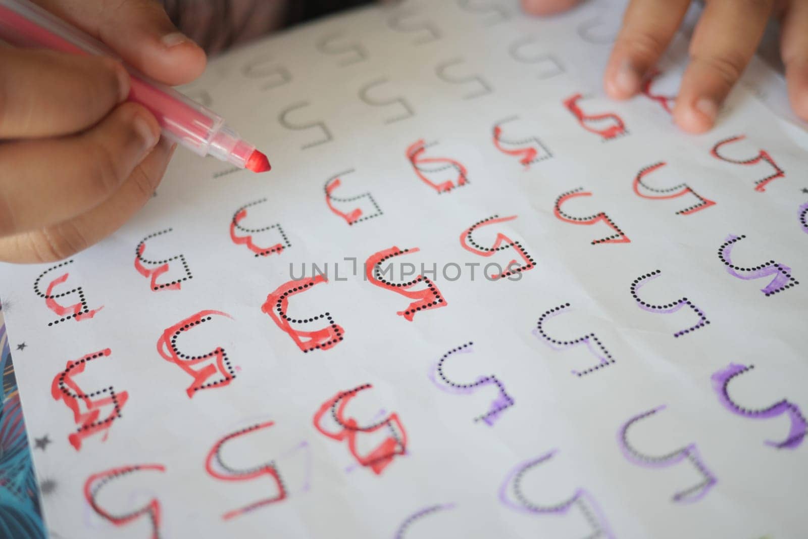 A child practices letter writing using markers on printed sheets.