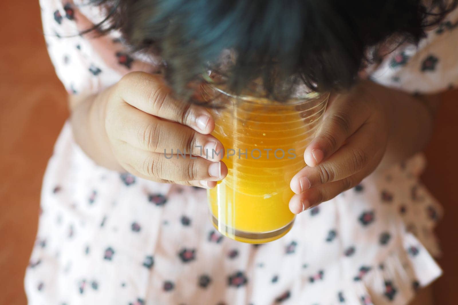 A young child holds a glass of orange juice while looking down, smiling.