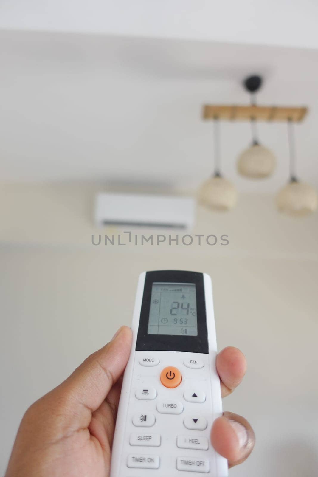 Hand holds a remote control while aiming at an air conditioner.