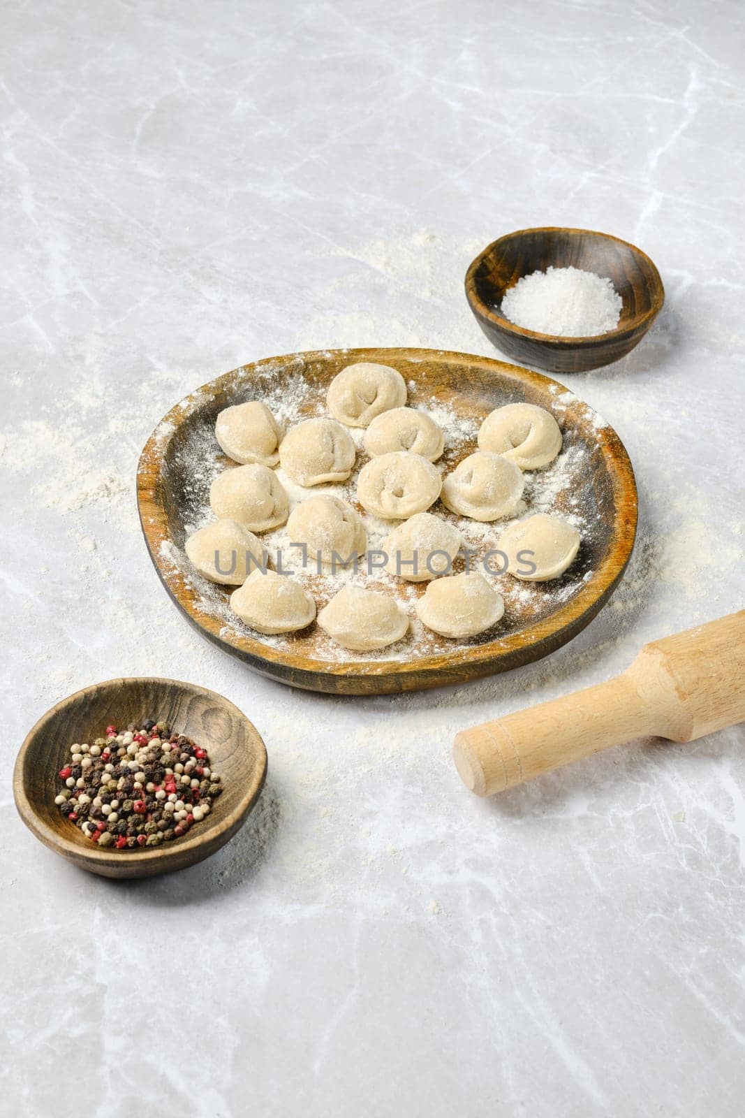 Dumplings on a wooden plate, sprinkled with flour, along with small bowls of salt and mixed pepper. A rolling pin rests beside them, highlighting the preparation process.