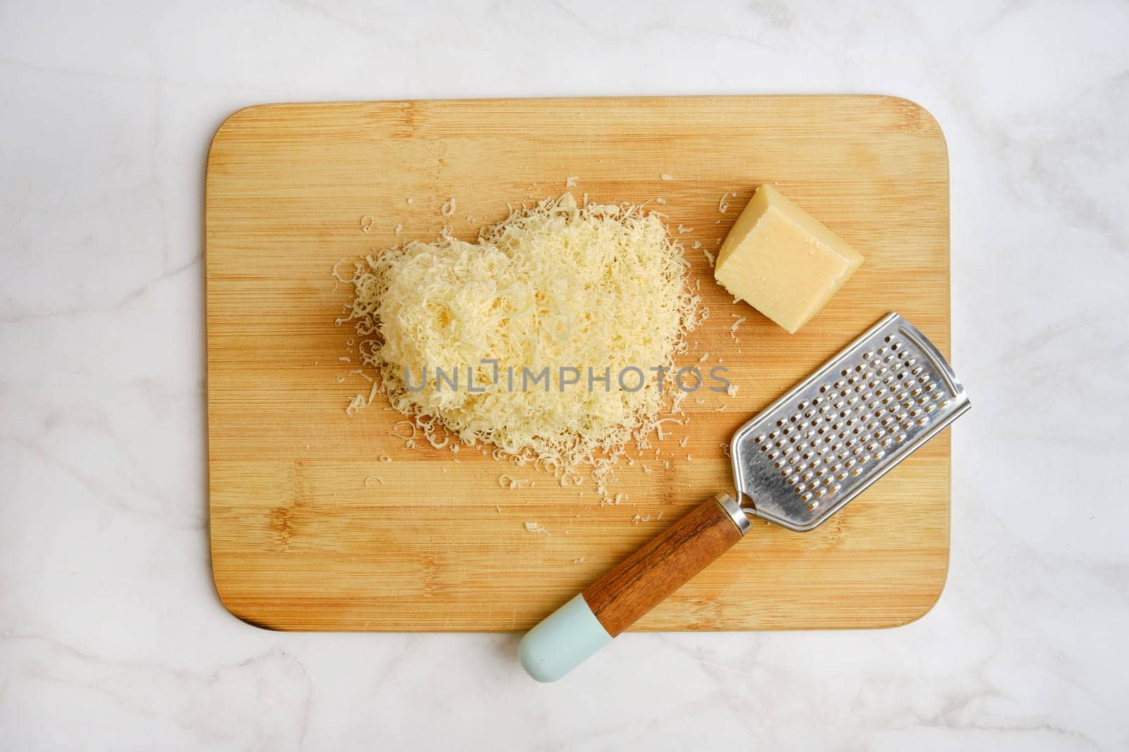 Shredded cheese on a wooden cutting board alongside a block of cheese and a grater. The items are arranged neatly in a well-lit kitchen, suggesting preparation for a delicious meal.