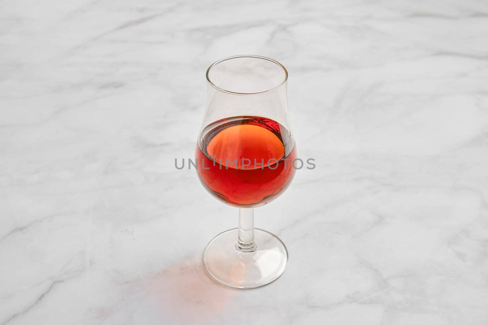A crystal-clear glass filled with a rich brandy on a smooth marble surface. Natural light reflects off the glass, enhancing its color and creating an inviting ambiance.