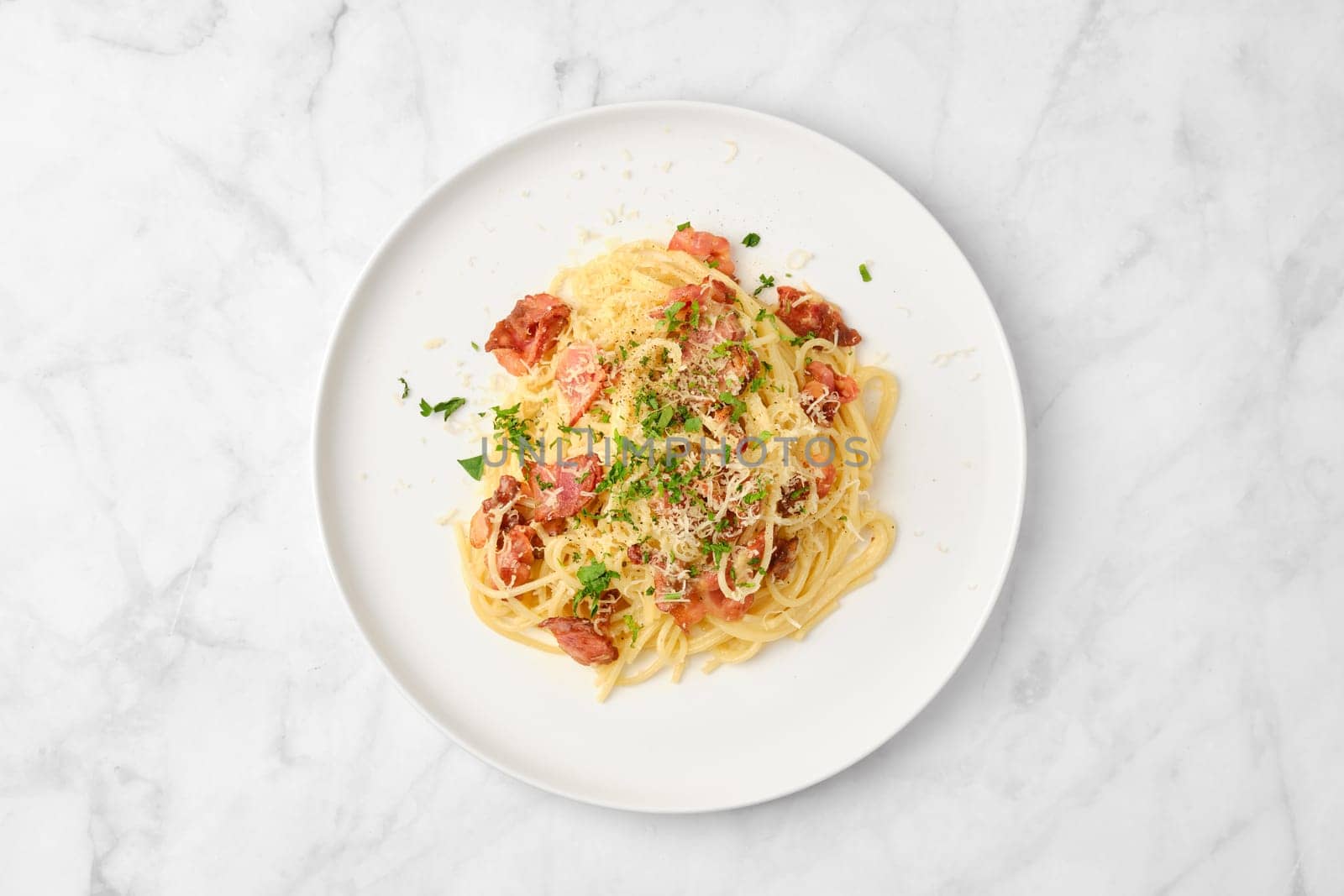 A bowl of spaghetti topped with crispy bacon and grated cheese sits on a clean, white plate. Fresh parsley garnishes the dish, creating an appealing presentation ready to be enjoyed.