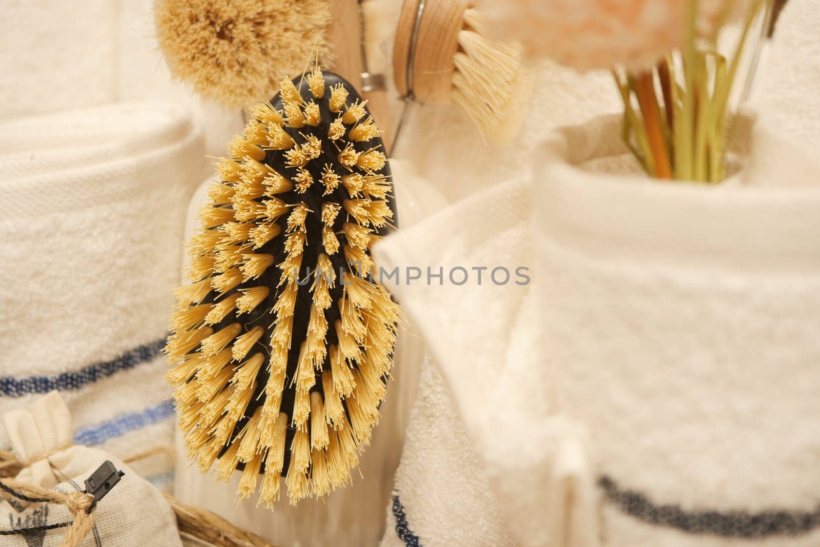 A natural cleaning brush hangs among towels and decorative items in a bathroom.