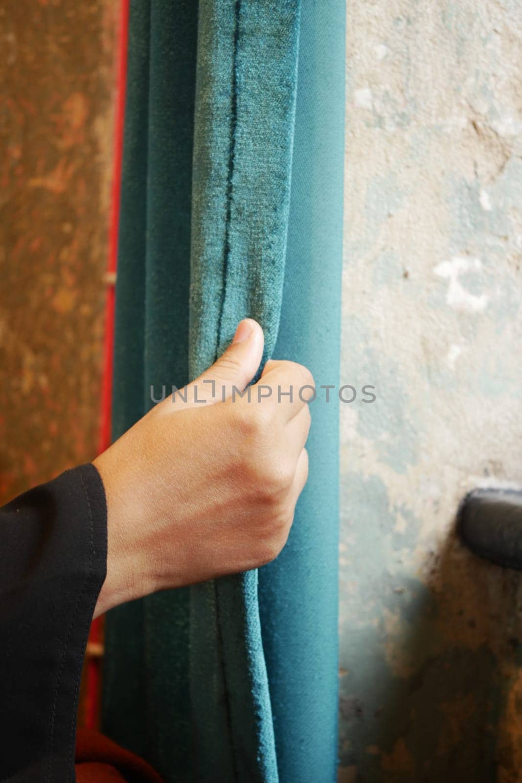 A hand pulls a soft blue curtain in a charming, textured room.