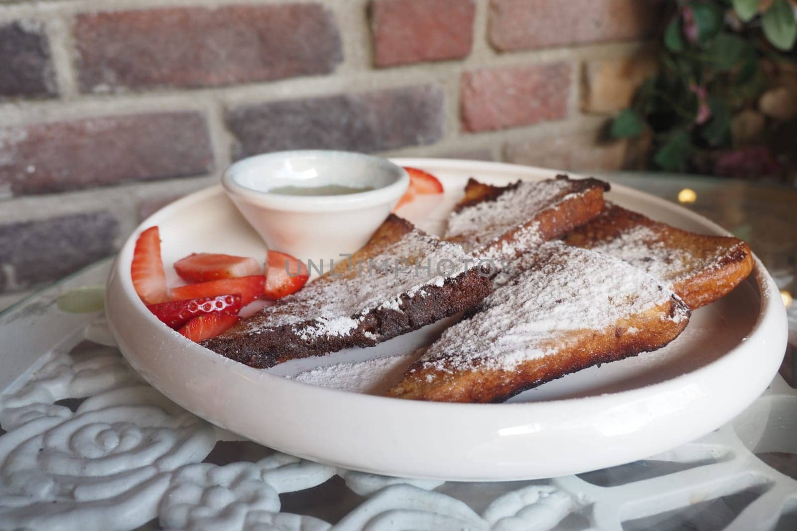 A plate of French toast garnished with powdered sugar and strawberries.