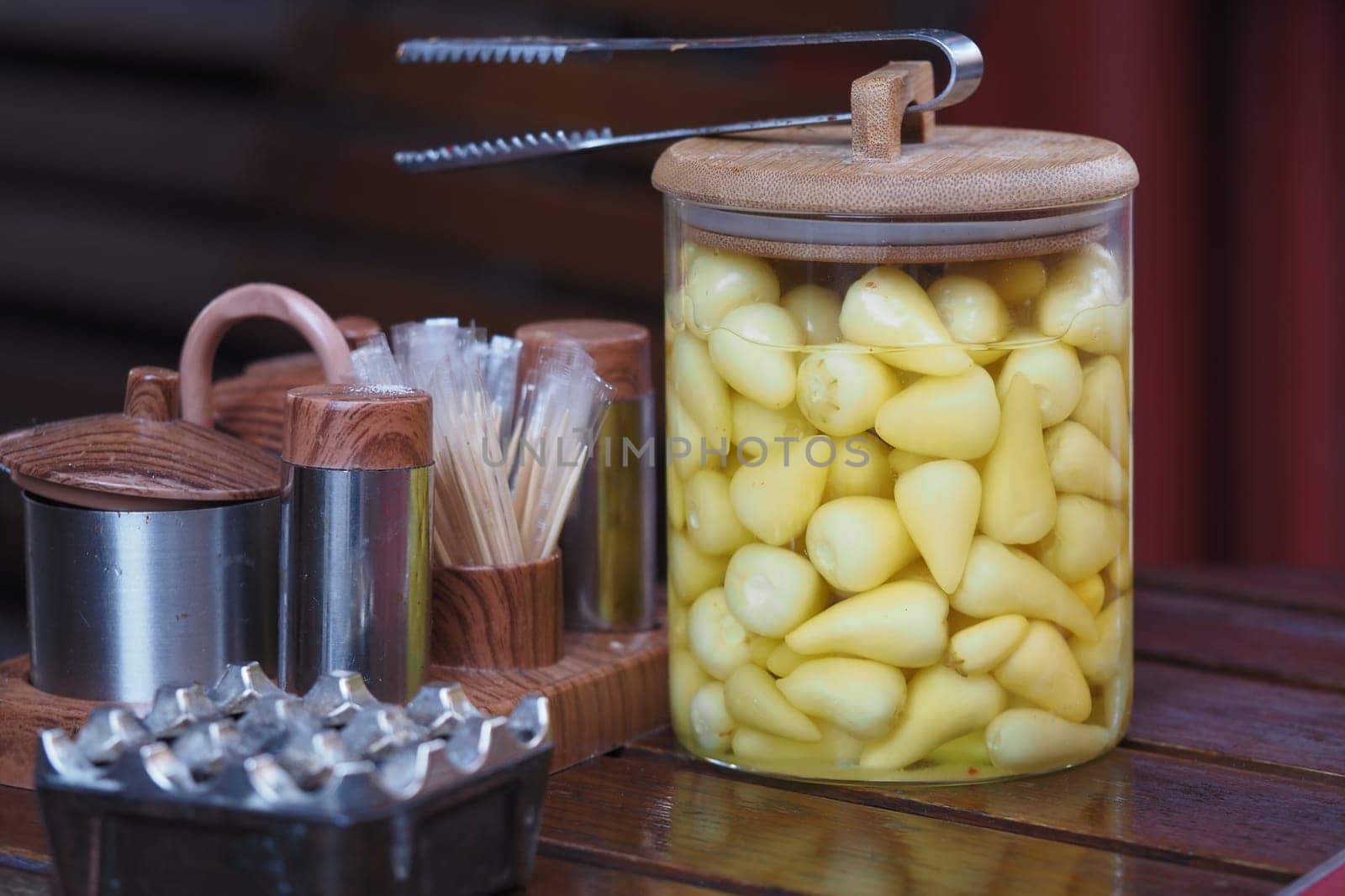 Yellow cloves of pickled garlic are displayed in a jar with utensils nearby.