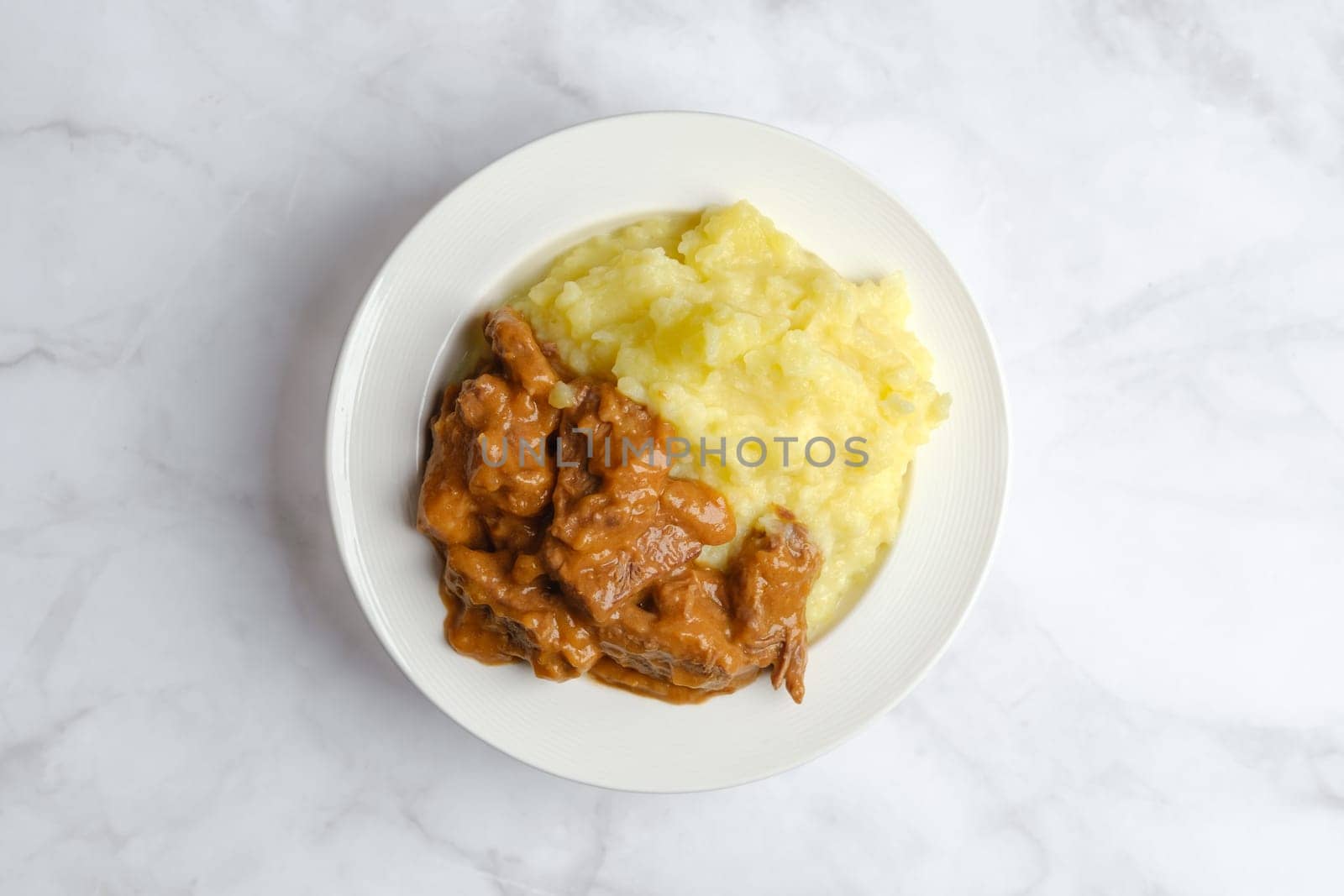 Overhead view of plate with beef goulash with mashed potato in a deep plate on marble background