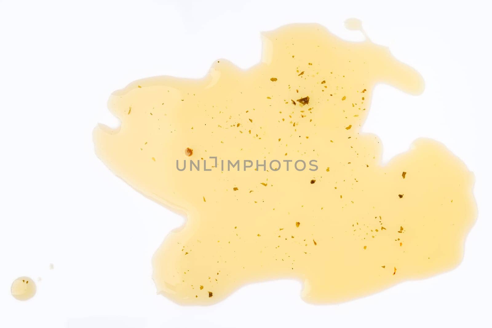 Olive oil with herbs is spread across a white surface, featuring dark specks that add visual interest.