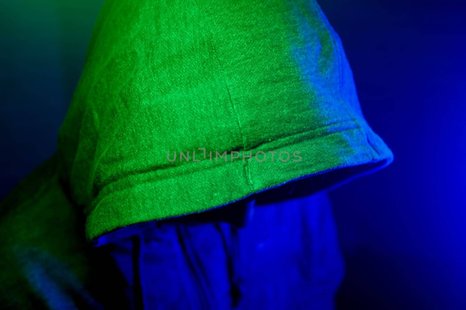 A figure in a hooded jacket is illuminated by colorful lights at night.