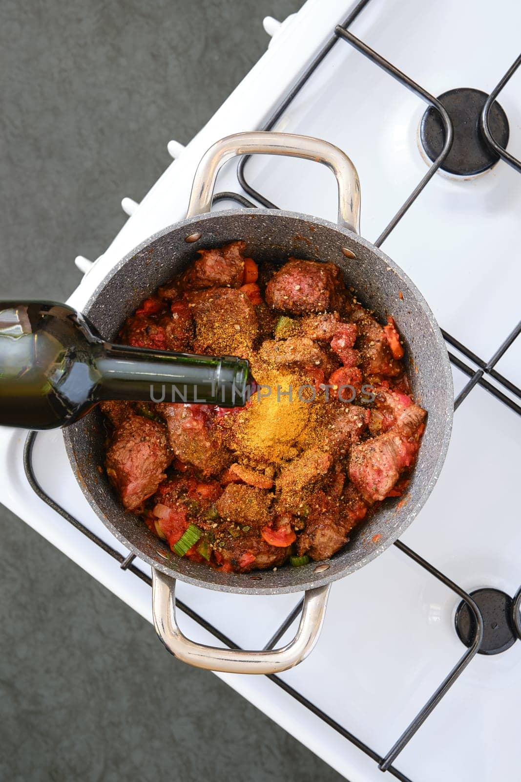 A pot filled with diced meat, chopped vegetables, and spices is being prepared on a sleek stovetop. Red wine is gently poured in to enhance flavours, creating a deliciously aromatic meal.